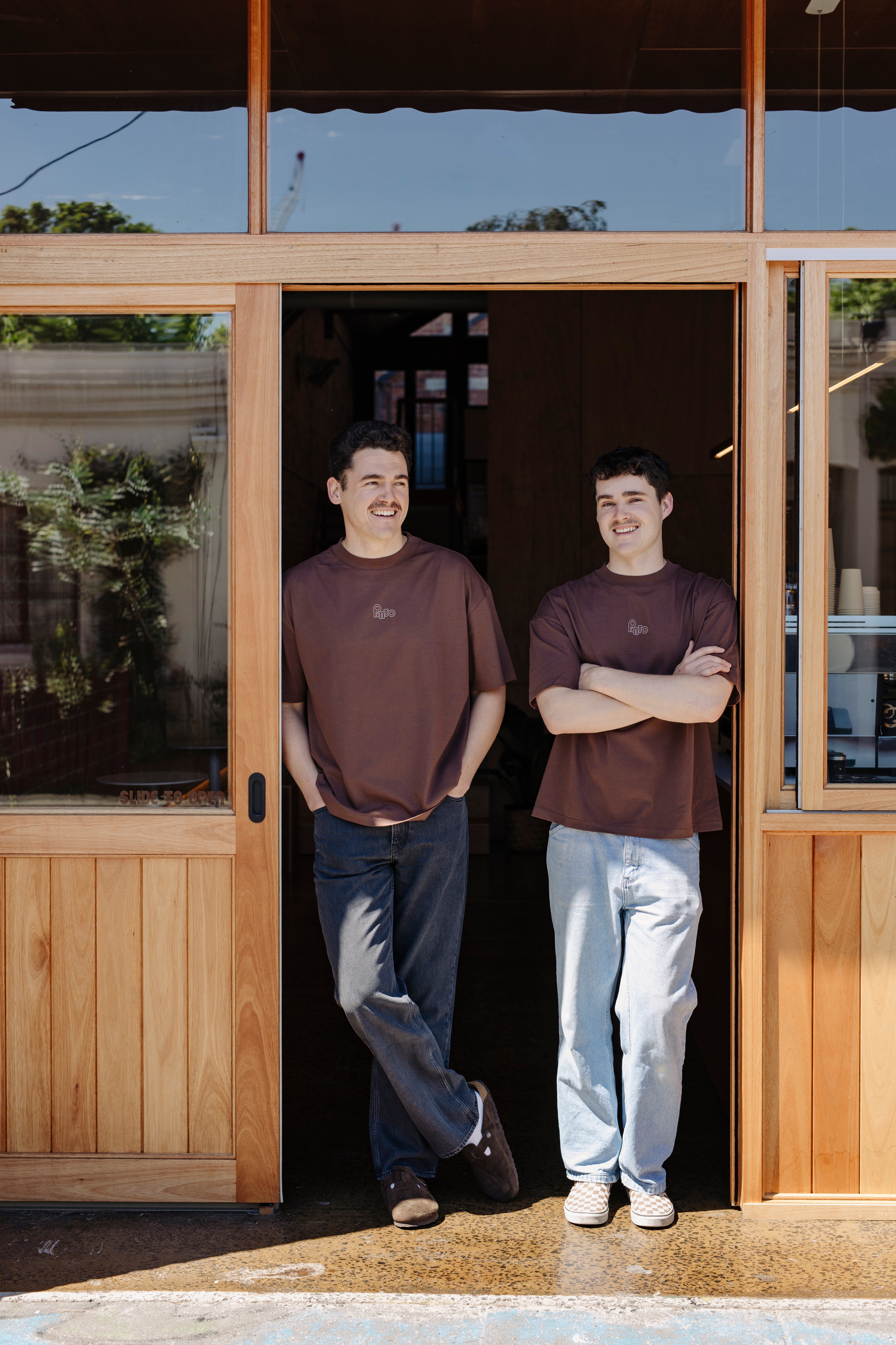 Two men standing outside a wooden building with glass doors.